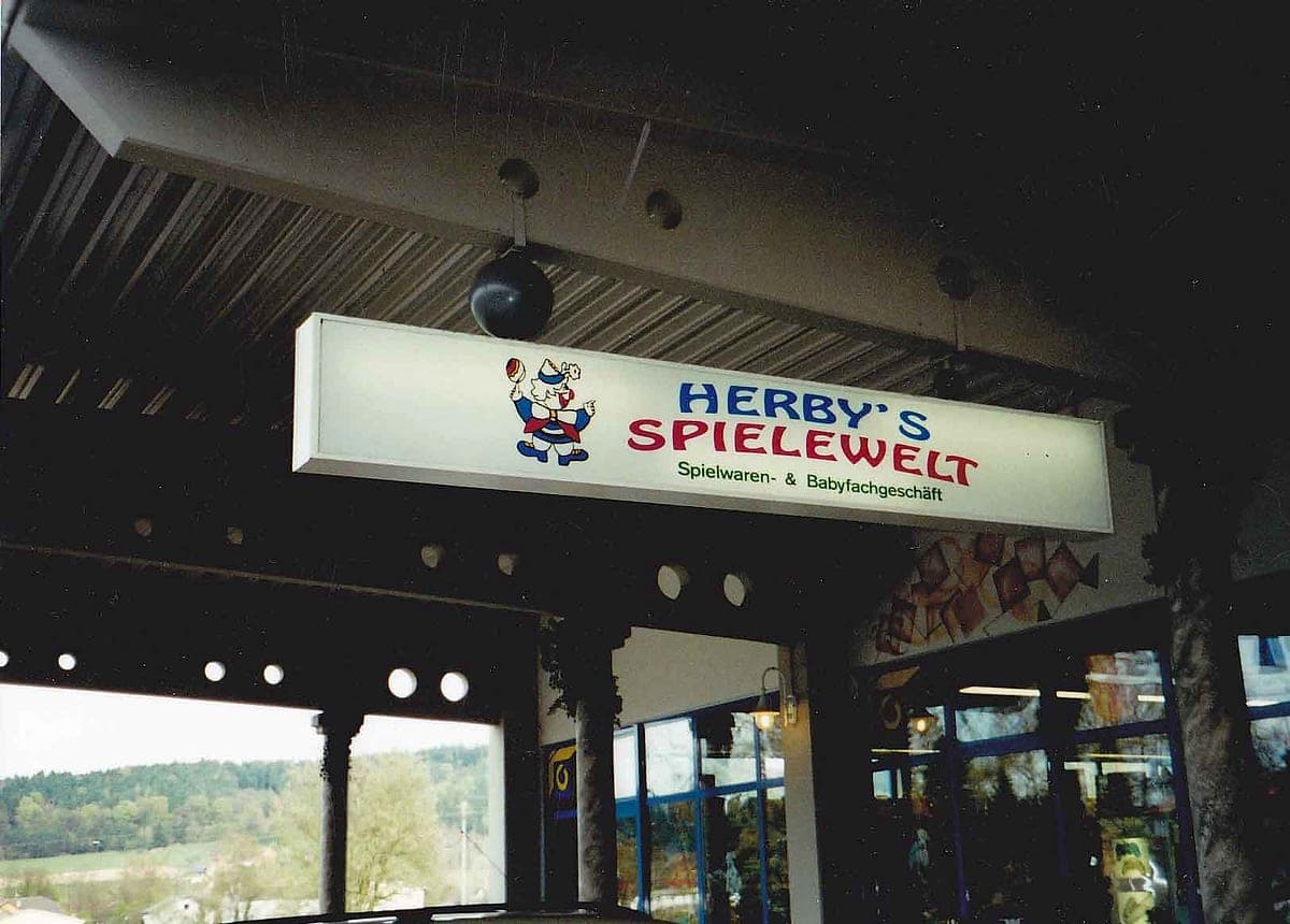 Eingang des ersten Geschäftslokals von Herby's Spielewelt mit Schriftzug „Spielwaren & Babyfachgeschäft“