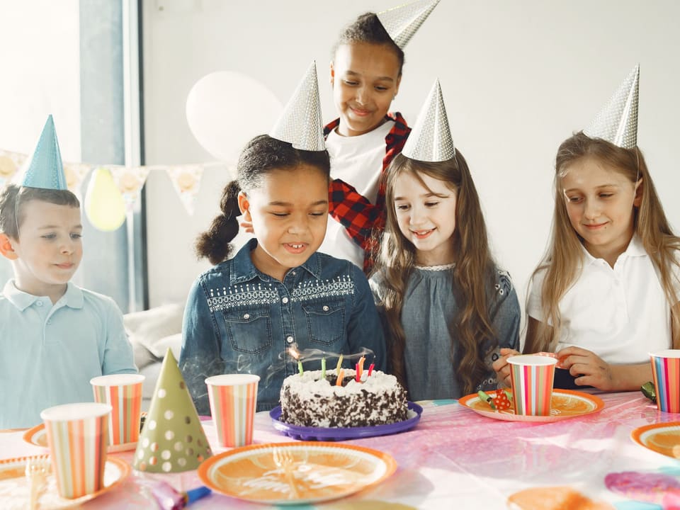 Kinder feiern mit Partyhüten an einem Geburtstagstisch