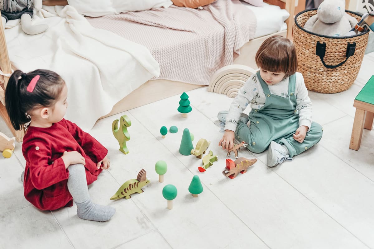 Zwei Kinder spielen auf dem Boden mit Holzspielzeug